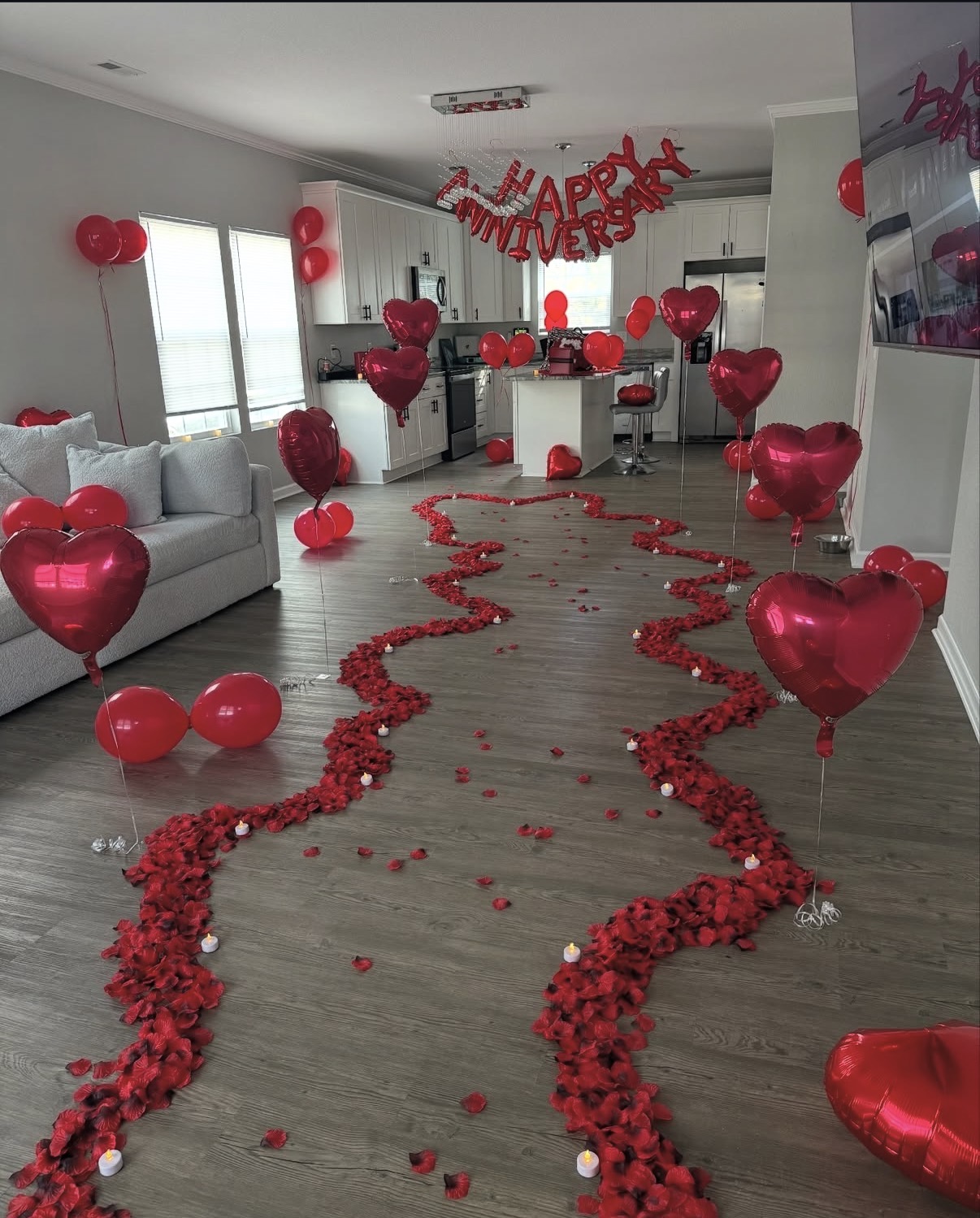 Red heart balloons, rose petals, candles, and Happy Anniversary balloons arranged throughout a room